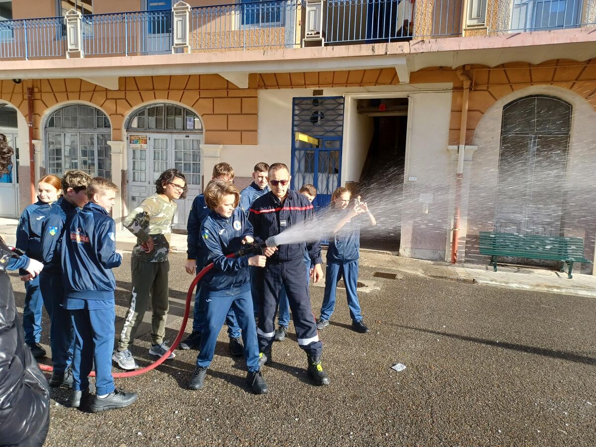 Des cadets manient une lance à incendie avec un sapeur-pompier