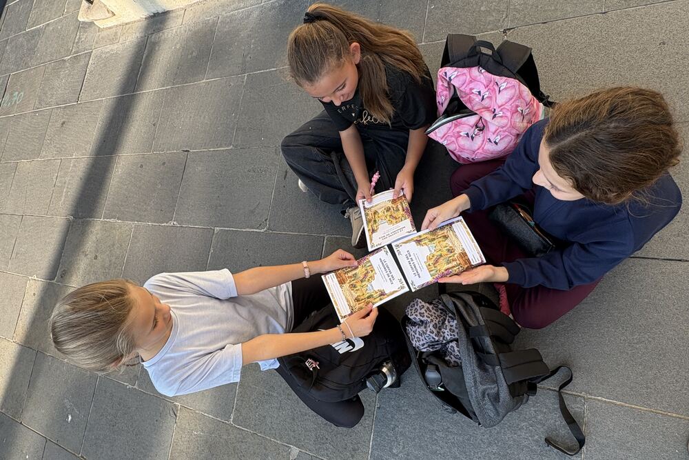 Trois élèves assises au sol feuillettent des livres