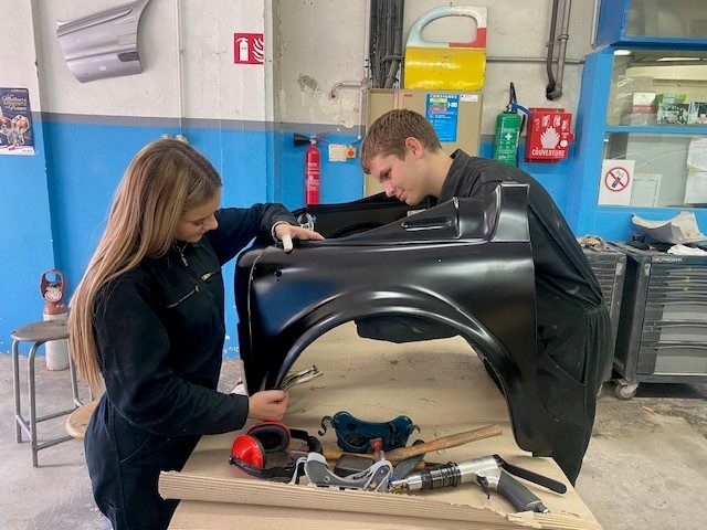 Une élève et un élève remettent en forme une aile de voiture à l’atelier de carrosserie