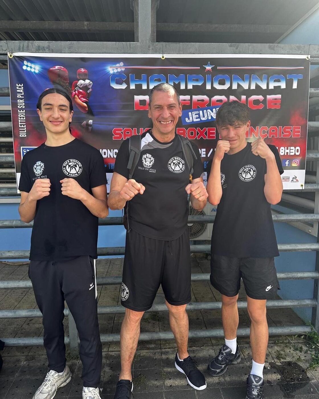 Deux jeunes sportifs et leur entraîneur devant l’affiche du championnat de France jeunes