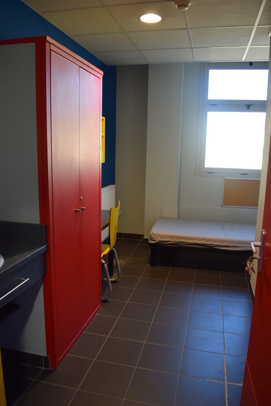 Une chambre de l’internat : bureau rouge, fenêtre et lit