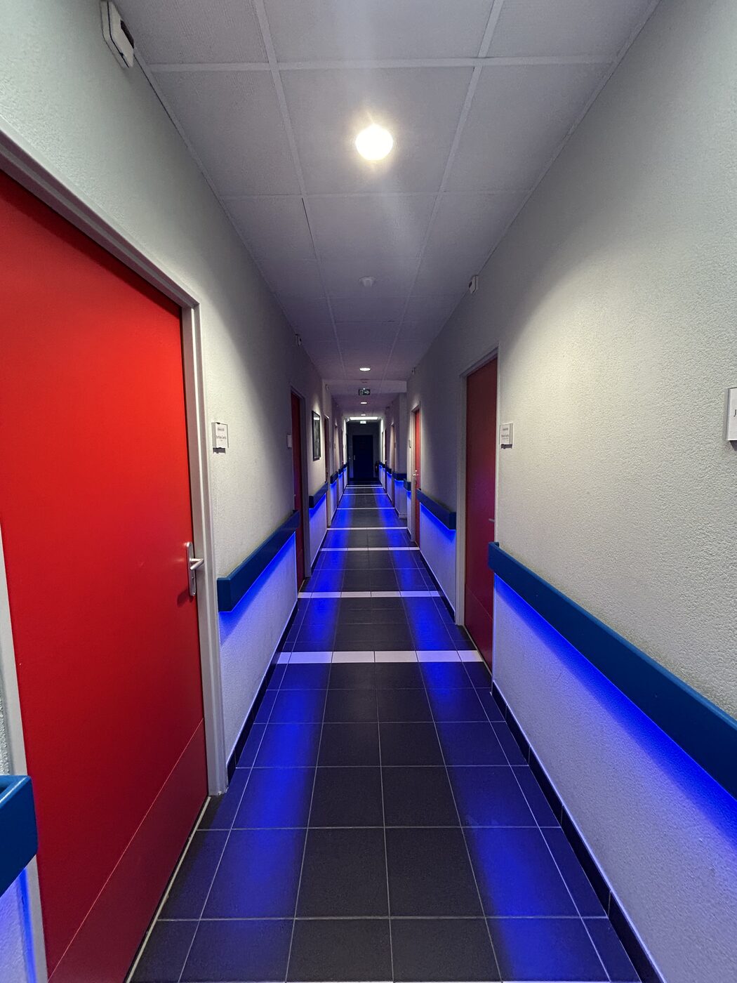 Un couloir de l’internat, éclairé de bleu, portes rouges