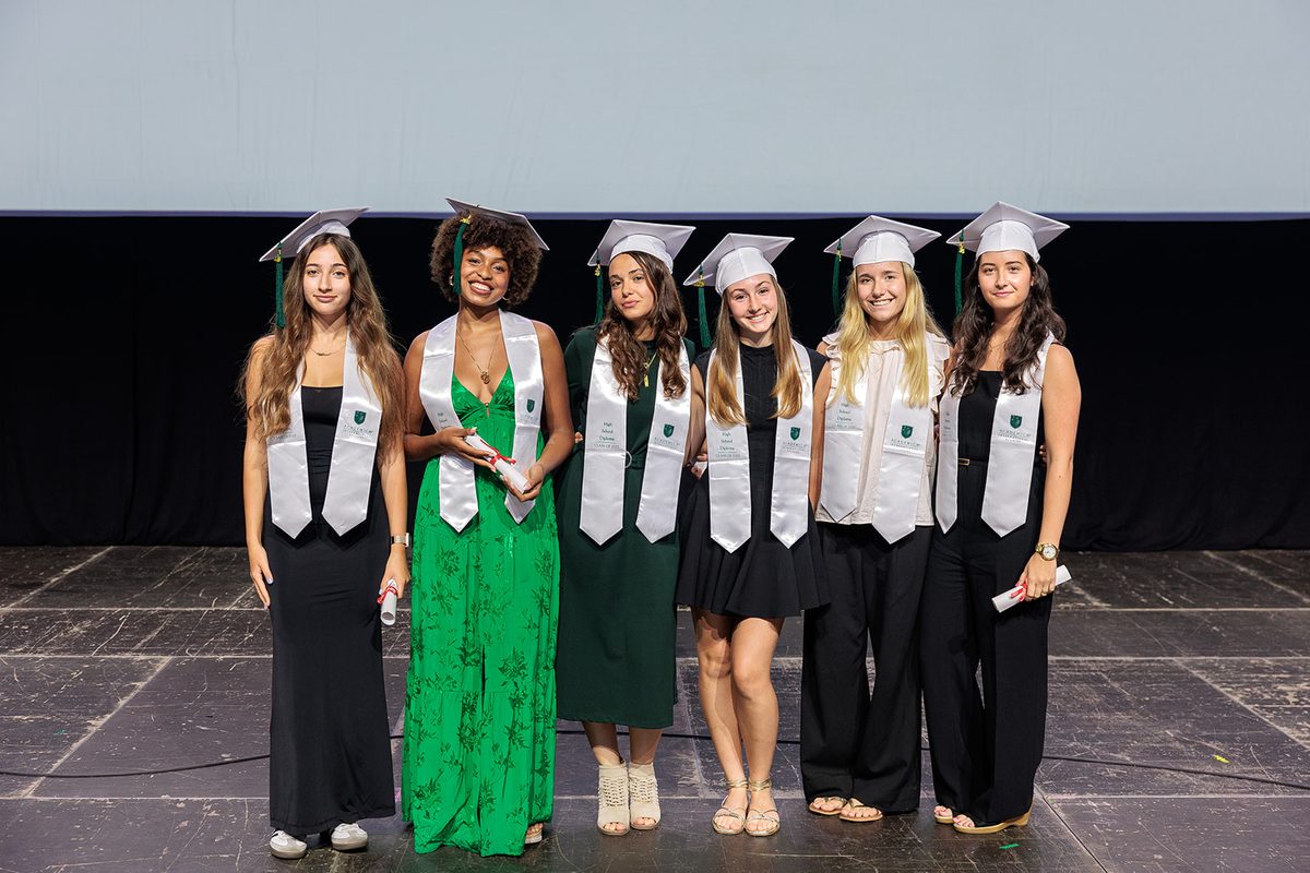 Six diplômées du Dual Diploma, toque et étole, sur la scène de la remise des diplômes
