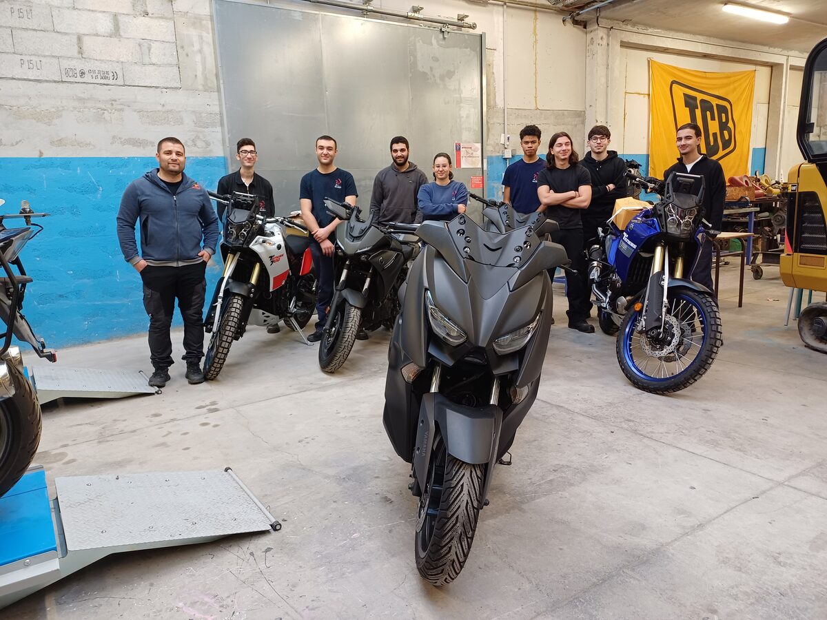 Élèves de l’option motocycles et leur formateur autour de motos et d’un scooter, à l’atelier