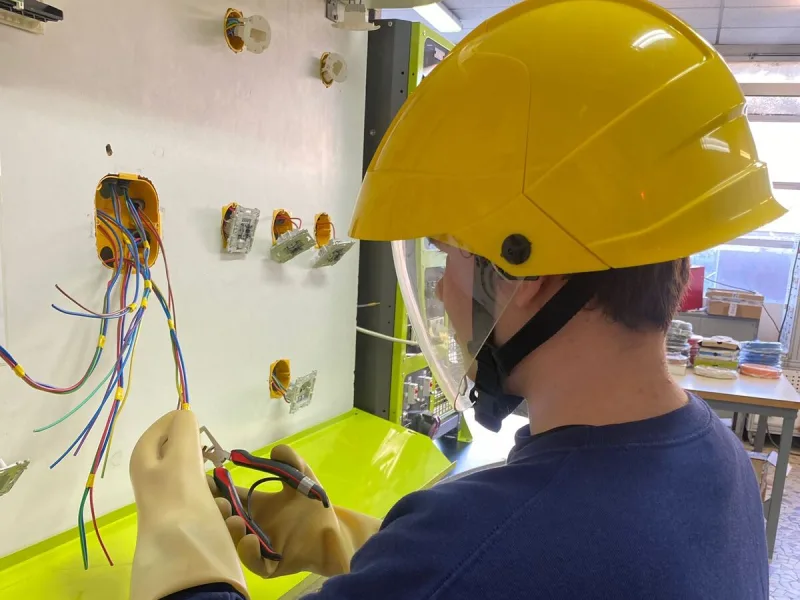 Un élève casqué câble un tableau électrique en atelier d’électrotechnique